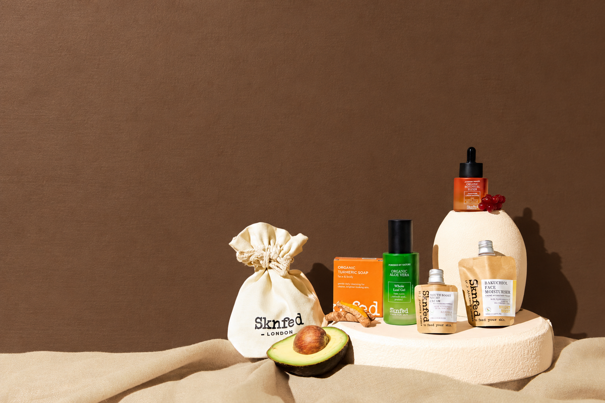 Sknfed natural skincare products arranged on warm stone plinths against a cocoa brown background